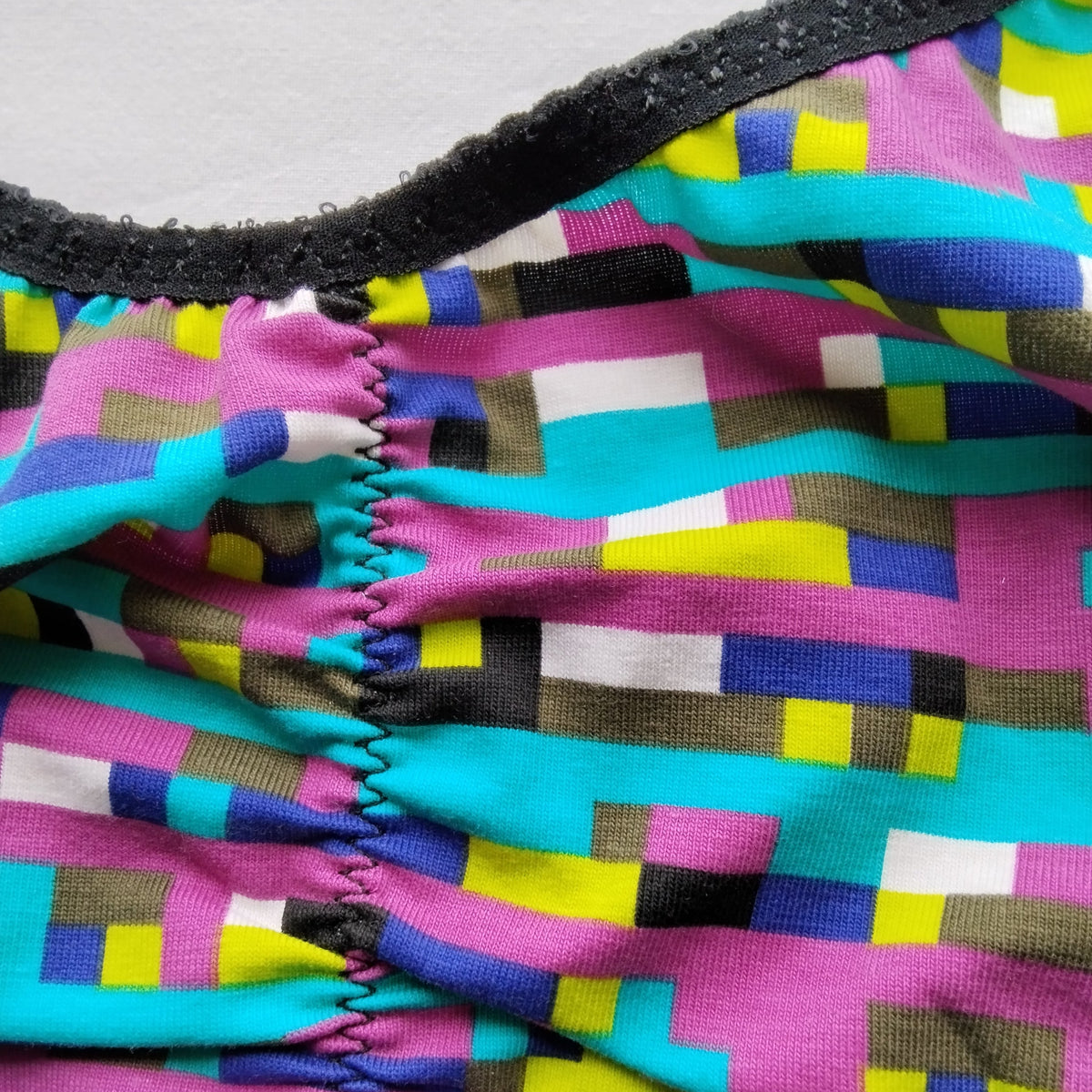 Gros plan sur le tissu et la couture centrale de la brassière artisanale taille 3XL motif pièce manquante – carrés colorés et finitions dentelle noire – création Grosse Patate Création